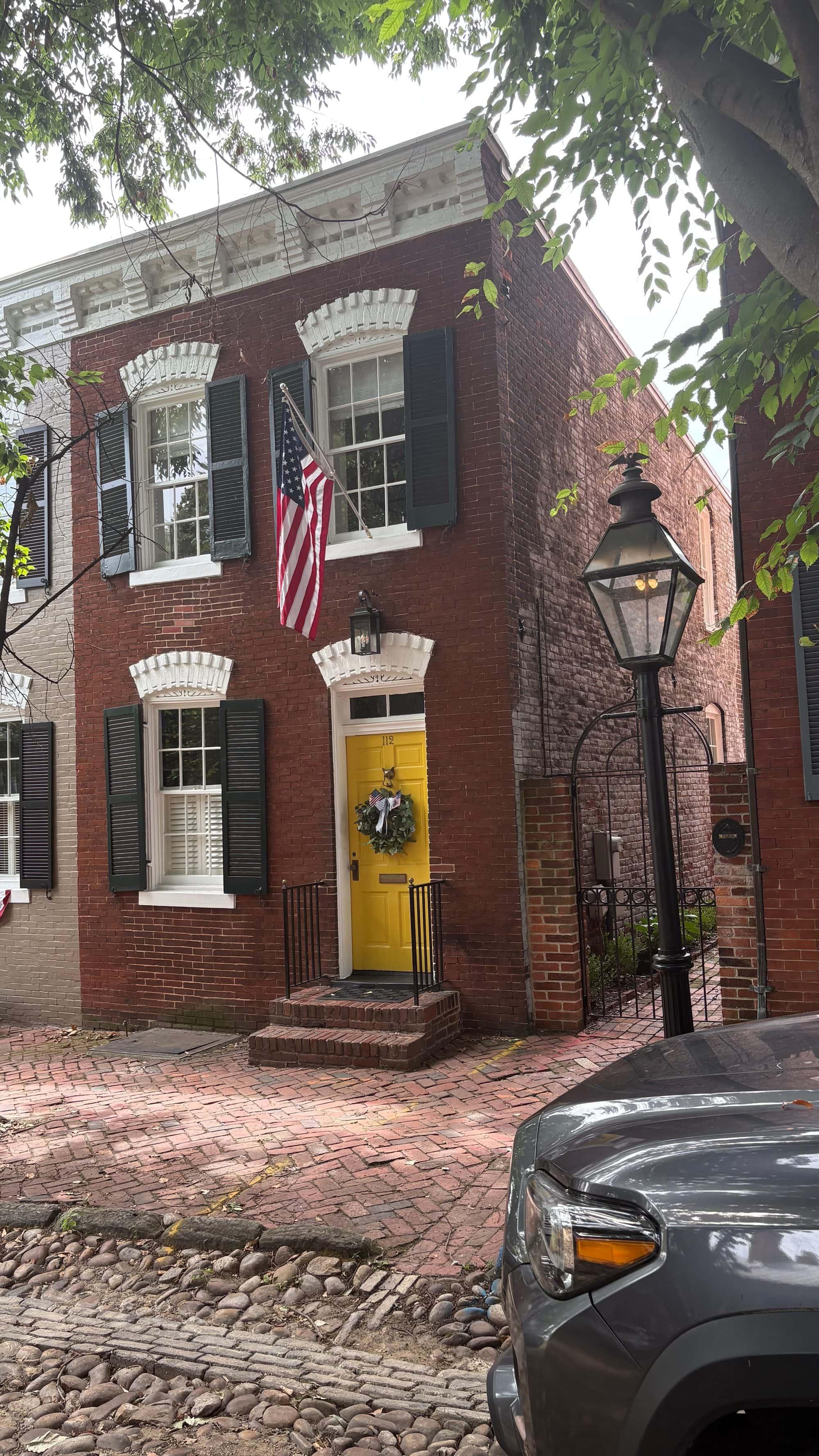 A classic yellow door with a wreath and American flag on a red-brick Old Town Alexandria rowhouse