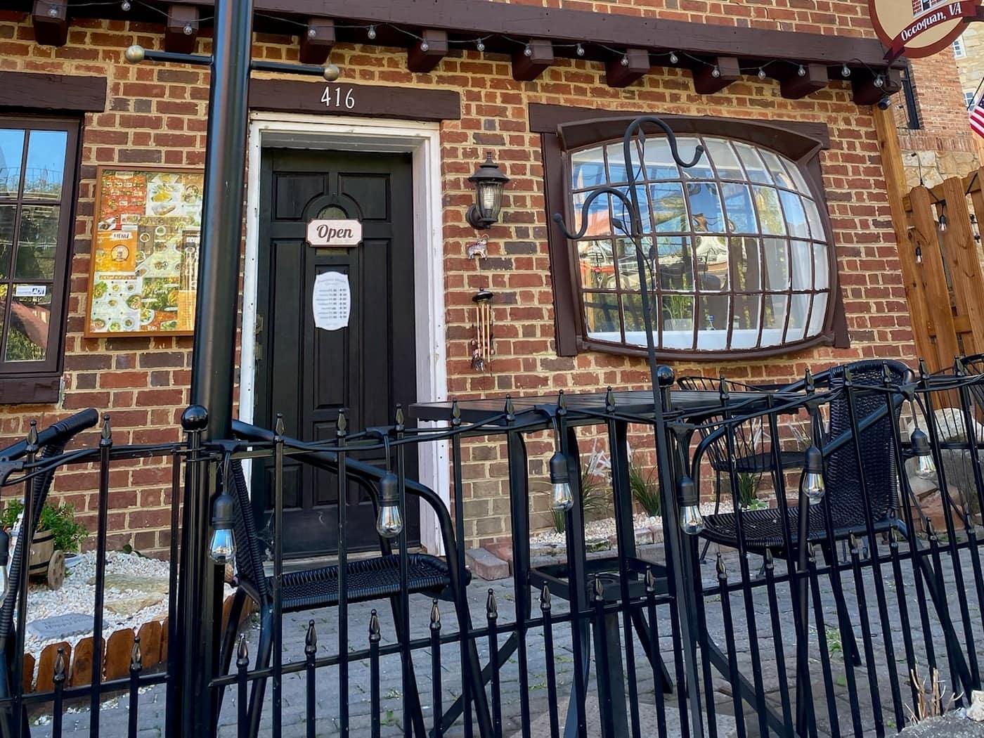 A brick storefront's door and café patio on Occoquan's Mill Street, string lights overhead
