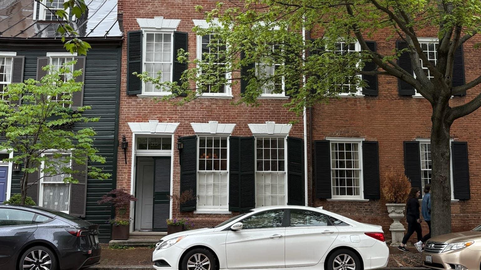 A quiet, tree-lined street of brick rowhouses in Old Town Alexandria on a spring afternoon
