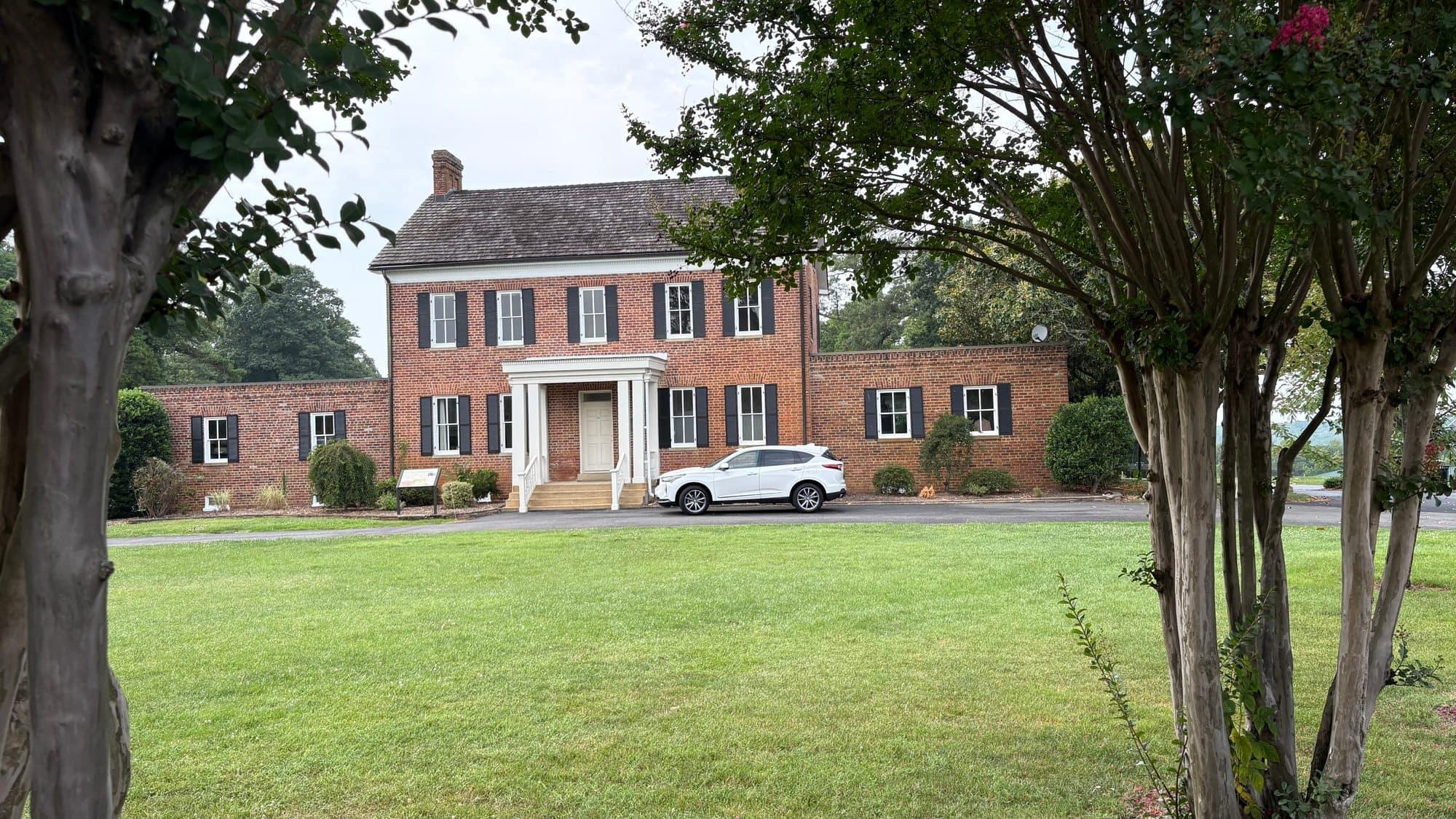 A stately brick colonial manor home with a white portico, set behind a wide lawn