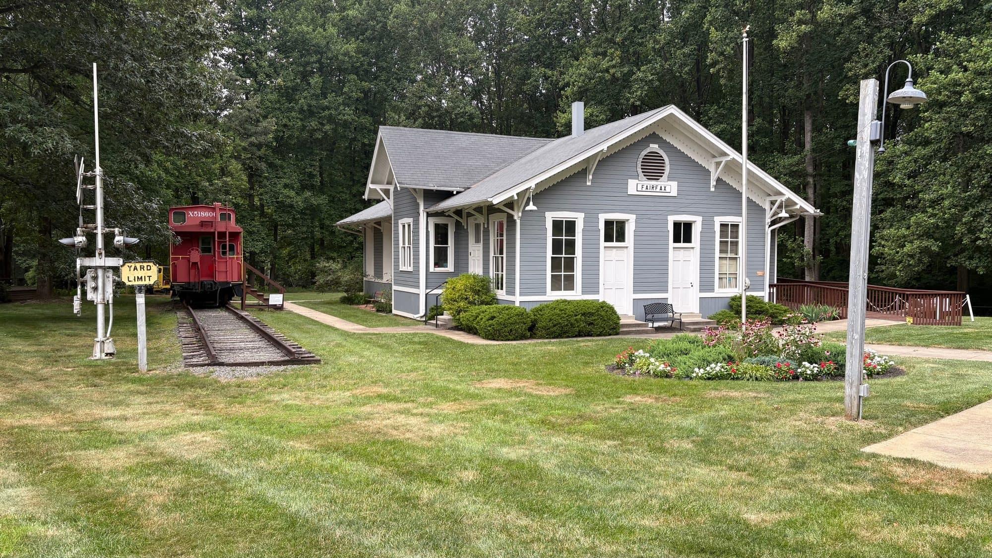 The historic Fairfax Station depot building with a restored red caboose on the tracks, surrounded by mature trees