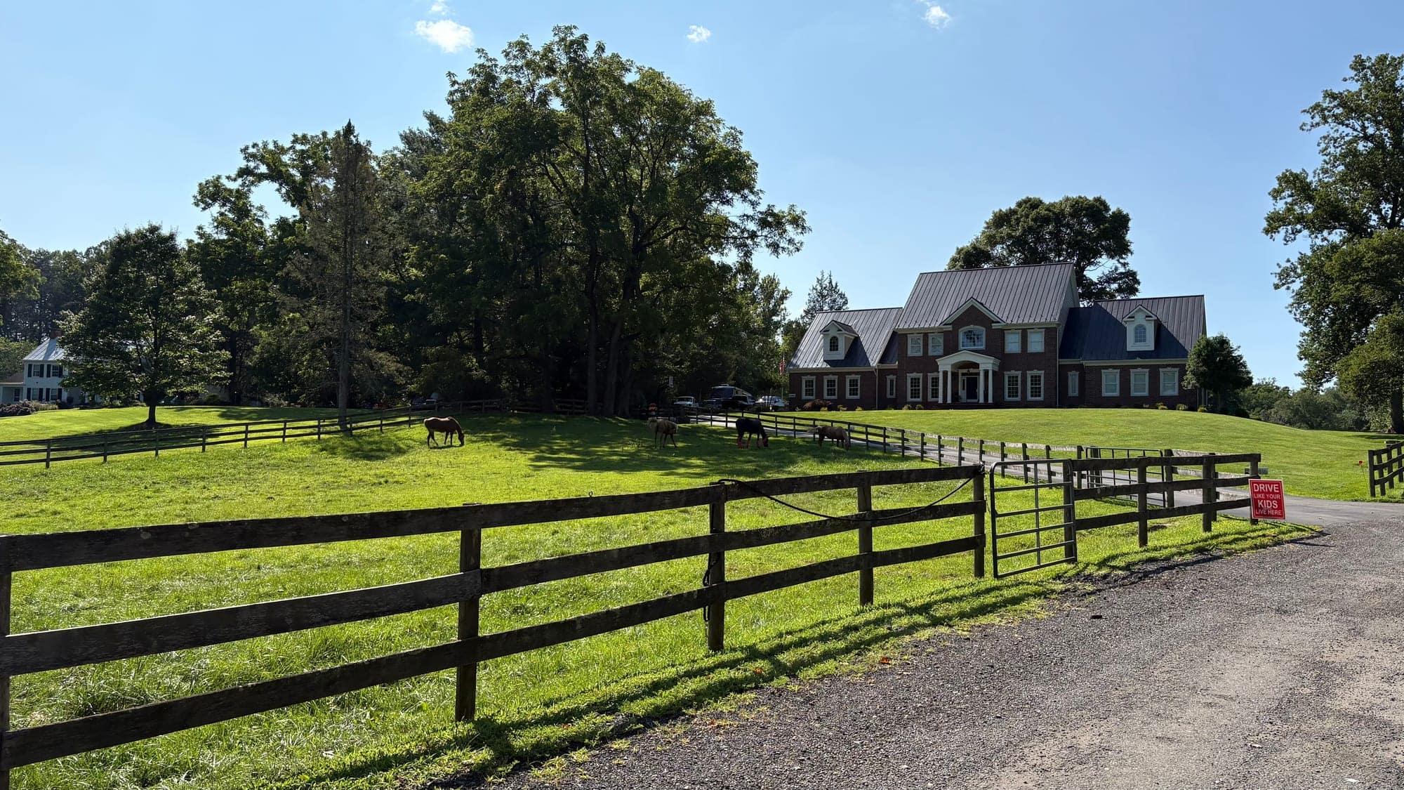 Horses grazing on a board-fenced pasture below a brick colonial home on a wooded Fairfax Station property