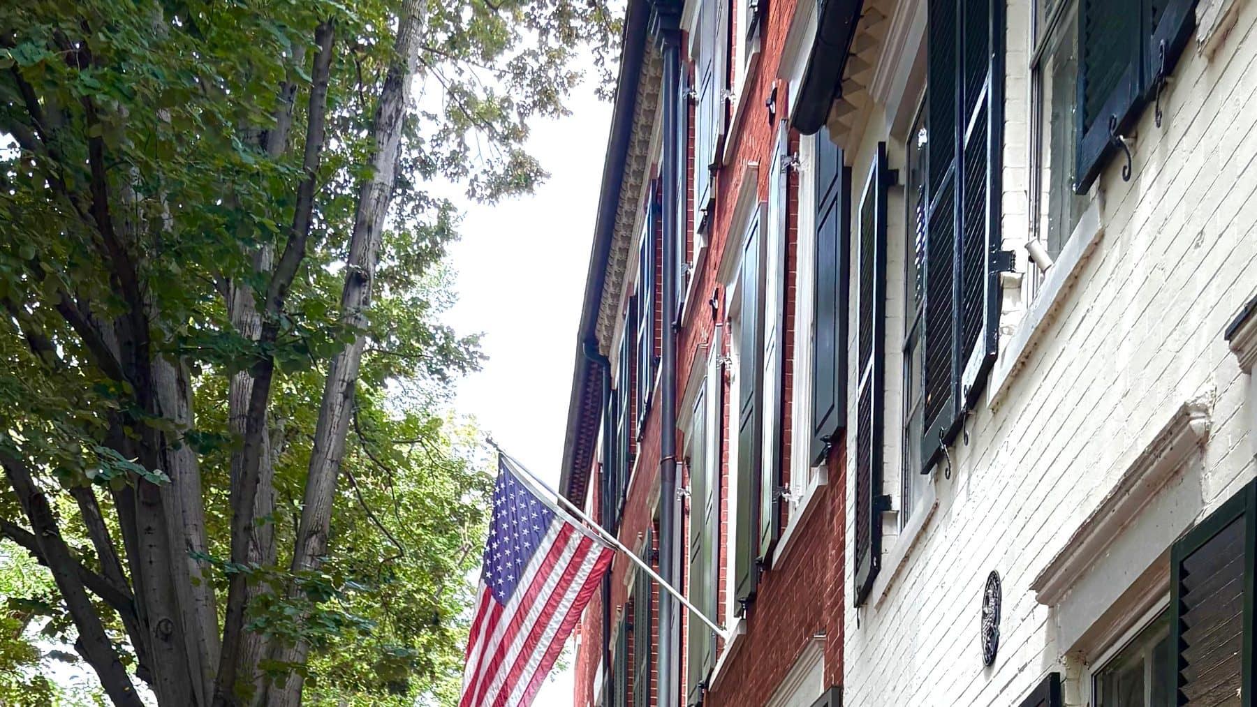 A tree-lined brick sidewalk in Old Town Alexandria leading past historic rowhouses, American flags overhead